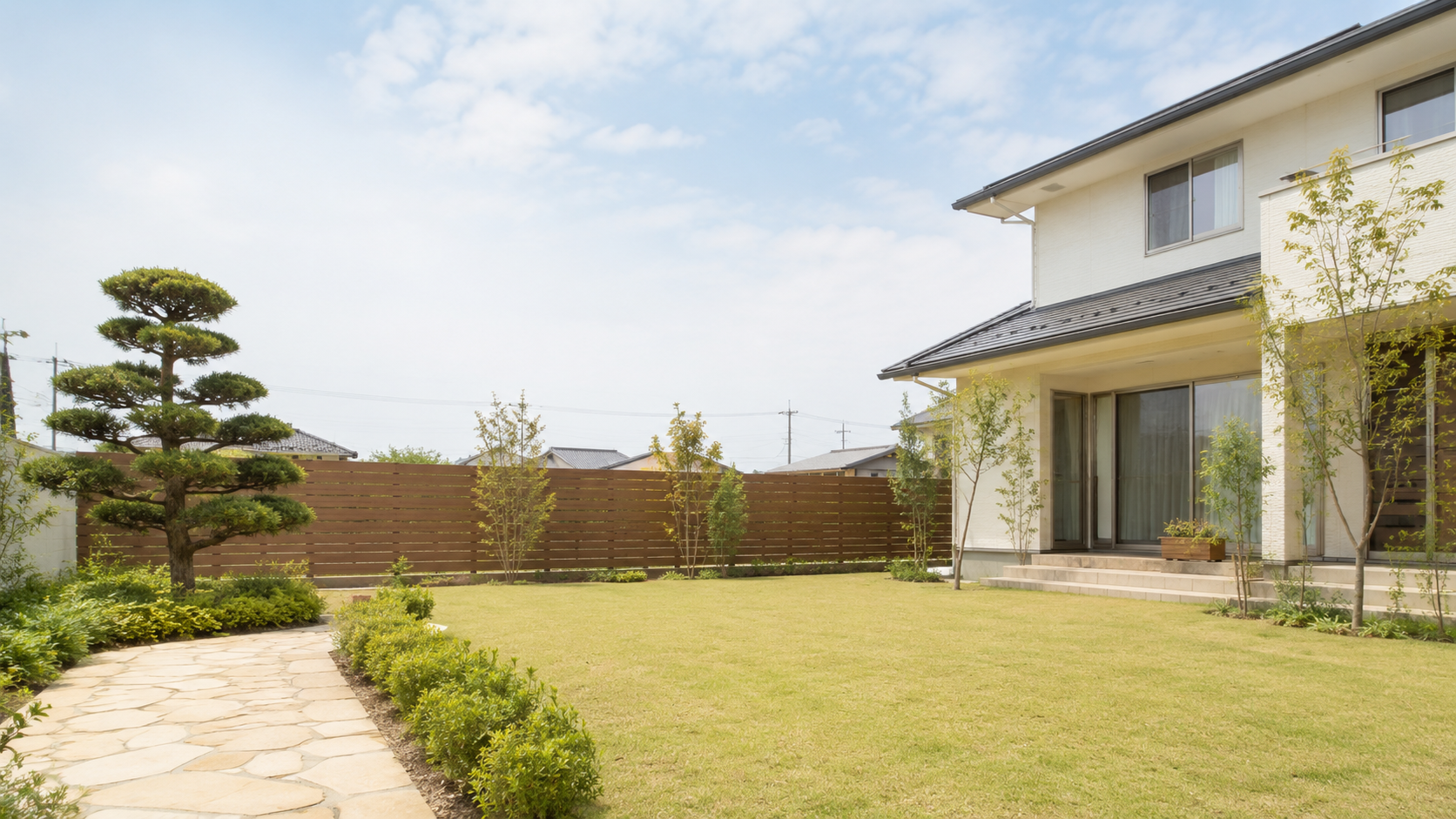 刈り揃えられた芝生と平板石のアプローチが整えられた、戸建て住宅の庭